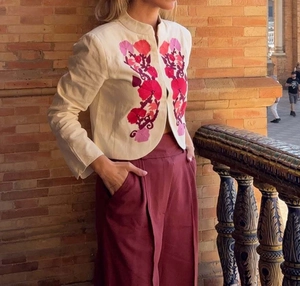 Close-up of elegant floral embroidery on beige jacket paired with burgundy trousers