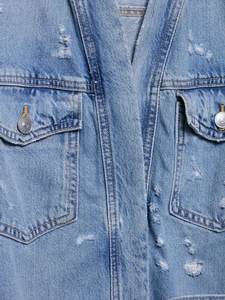 Close-up of light blue denim jacket featuring distressed details and metal button pockets
