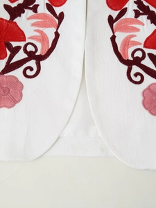 Detailed close-up of white blazer hem featuring intricate red floral embroidery details