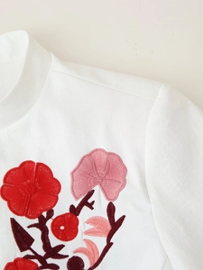 Close-up of intricate red floral embroidery on the white minimalist blazer jacket