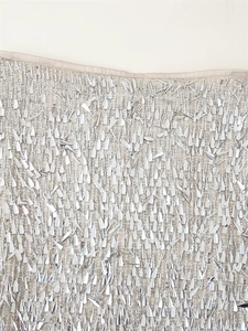 Close-up detail of silver sequins and metallic beads on a beige fabric skirt