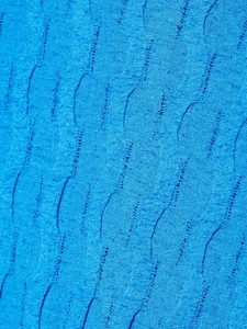 Macro detail of royal blue cable knit texture with wave pleats and distressed hollow design