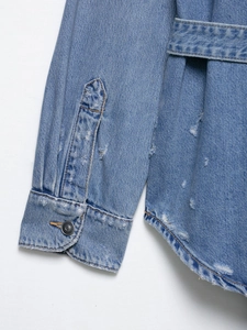 Detail of distressed denim jacket featuring ripped sleeve cuffs and a matching waist belt