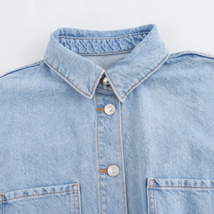 Dettaglio tutina in denim celeste con bottoni argentati, colletto a punta e cuciture arancioni