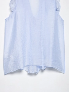 Close-up of light blue sleeveless top featuring satin texture and ruffle shoulder detail