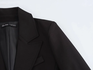 Detailed view of the brand collar label and padded shoulder on the black tailored jacket