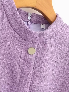 Détail macro du tissu en tweed violet avec bouton décoratif et col montant sophistiqué