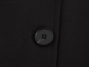 Detailed close-up of a matte black four-hole button on textured twill fabric garment
