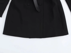 Detail view of the black mini dress hem featuring matching buttons and a slim waist belt