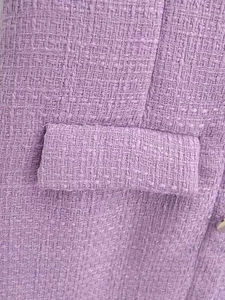 Détail macro du tissu en tweed lavande et du bouton métallique sur la robe chic