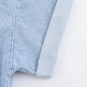 Dettaglio ravvicinato del tessuto denim azzurro e cuciture del risvolto sulla manica