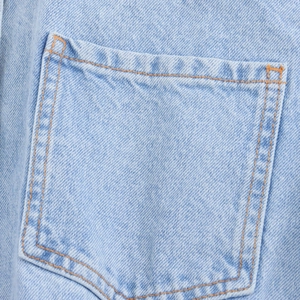 Dettaglio ravvicinato del tessuto denim azzurro con cuciture a contrasto arancioni e tasche