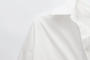 Close-up detail of smooth white fabric texture and collar stitching on long sleeve shirt