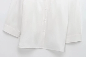 Detail view of the white long-sleeved shirt with single-breasted buttons and wide-cuff stitching