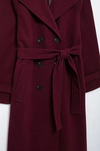 Detail of burgundy double-breasted wool coat featuring classic lapels and a matching belt