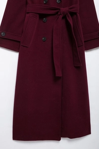 Detail of burgundy wool trench coat featuring double-breasted black buttons and tied belt