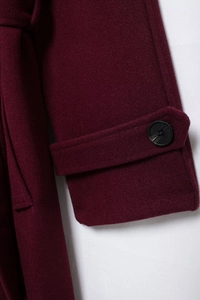 Detailed macro view of wine red wool coat cuff featuring tab and black resin button