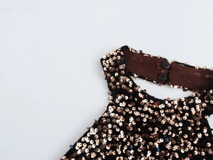 Detail of rose gold sequins on black fabric with halter neck button closure
