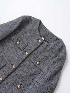 Detail of tweed texture and gold dome buttons on a classic round neck jacket