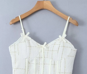 Détail d'un top caraco en tweed blanc avec nœuds décoratifs et texture à carreaux dorés