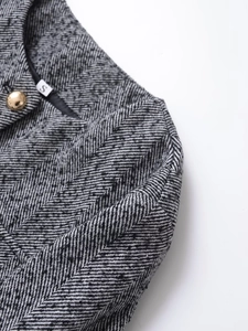 Detailed close-up of grey herringbone texture and gold button on elegant women's jacket