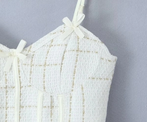 Gros plan sur le tissu en tweed blanc avec fils dorés et nœuds en satin sur le haut V