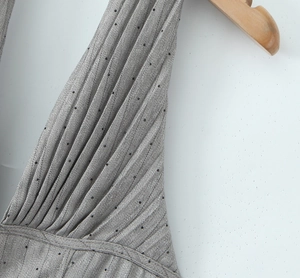 Detail eines grauen Satinkleids mit Faltenstruktur und kleinen schwarzen Punkten auf dem Stoff