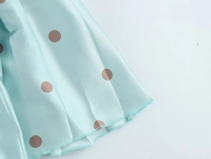 Détail d'une robe vert menthe à pois montrant la couture de l'ourlet et le tissu satiné