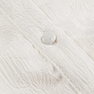Detail aus weißem Jacquard-Stoff mit floraler Textur und passendem Stoffbezogenem Knopf