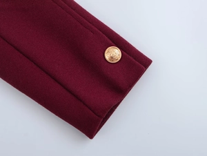 Detail of burgundy wool coat sleeve featuring an ornate gold crest metal button decoration