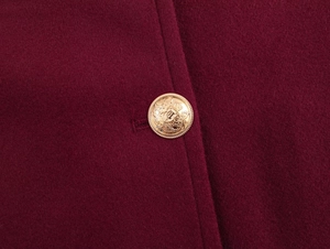Macro detail of high-quality burgundy wool coat featuring gold heraldic lion crest buttons
