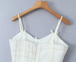 Détail d'un caraco en tweed blanc avec motif à carreaux dorés et structure corset