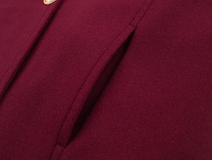 Detail of burgundy wool coat showing welt pocket and golden metallic button closure