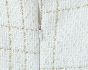 Détail du tissu en tweed blanc avec fils dorés et fermeture éclair invisible de qualité