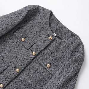 Close-up of textured black and white tweed jacket with gold dome buttons and round neckline
