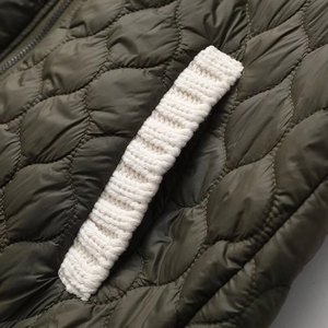 Detailed close-up of dark green quilted jacket with white knitted pocket trim and texture