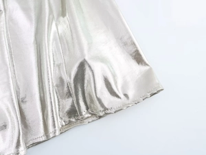 Detailed close-up of metallic silver fabric texture and fine stitching on the dress hem