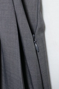 Dettaglio macro della cerniera invisibile su pantaloni grigi in tessuto plissettato