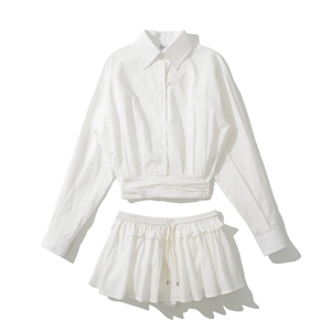 Flat lay of a white two-piece set featuring a cropped button-down shirt and ruffled skirt