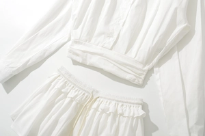 Flat lay of a white two-piece set featuring a button-down shirt and a drawstring ruffle skirt