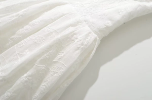 Detailed macro view of white floral embroidery and pleated texture on lightweight dress