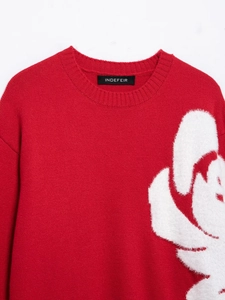 Close-up of red knit sweater featuring white plush floral appliqué and round neckline