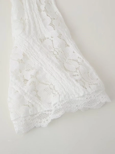 Détail d'une robe en dentelle blanche avec broderies délicates et bords ondulés