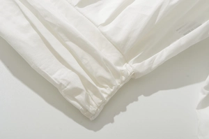 Detail of white cotton blouse with elastic cuffs and pleated hemline design