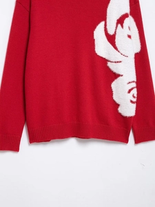 Detail of red knit sweater with white plush floral pattern and ribbed texture cuffs