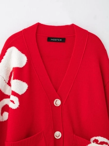 Detailed close-up of a red V-neck knit cardigan with marble buttons and white patterns