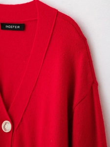 Macro view of the soft red knit texture, pearl button, and brand label on a V-neck cardigan