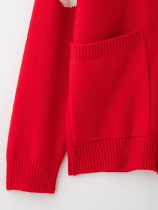 Detail of red knit cardigan featuring a large pocket and ribbed cuffs with plush trim