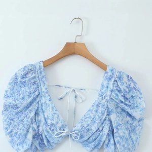 Light blue floral blouse with puff sleeves and tie-up detail on a wooden hanger