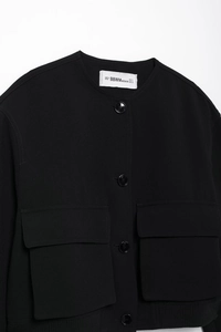 Detail of black crew neck cropped jacket showing large flap pockets and woven fabric texture